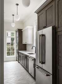 Sleek and functional, the scullery showcases an additional refrigerator and dishwasher, a deep sink, and custom cabinetry—framed beautifully by natural light pouring in from the window beyond.