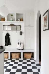 A black-and-white checkerboard cement tile floor leads the way through this fully customized mudroom featuring a stunning quartz bench.