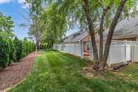 Green space behind patio with mature landscaping and shade.