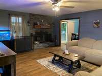Cozy living room with ceiling fan, wood burning fireplace, and hardwood floors.