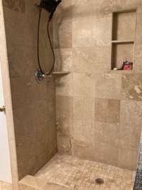 Fully tiled shower and tiled nook for shower essentials in primary bathroom..