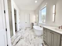 The primary bathroom is a study in grand design, with its expansive layout and sleek design, creating a sense of space and serenity. At the heart of the primary bathroom is a luxurious soaking tub, a centerpiece of relaxation and indulgence.