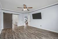 Primary bedroom features a tray ceiling, luxury vinyl plank floors and a barn door leading in to the primary bathroom and walk in closet