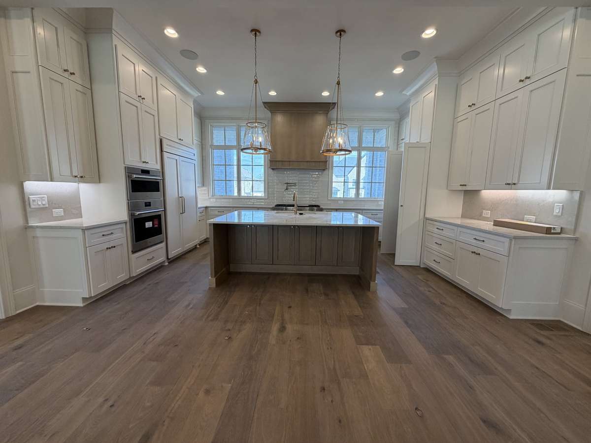 Spacious gourmet Kitchen with Wolf appliances including three ovens, a hidden pantry, quartz countertops, backsplash, and a flush island. 
Photo taken: 3/20/26