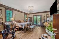 The main bedroom of this Gothic home is a romantic retreat with French doors framed in dark wood step into a private terrace that overlooks the kidney shaped pool
