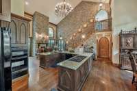 Kitchen cabinetry is crafted with elegant arched panels. The rugged stone wall lined with sconces provides a warm unexpected contrast to the beauty of both materials.  The kitchen is both a functional space and a experience of historic cozy warmth.