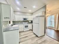 Kitchen has white cabinets w/crownmolding; quartz countertops with tile backsplash  and white appliances ; recessed lighting overlooking Eat in area and Separate Dining Room;