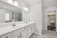 Primary bath has tile flooring, crown molding, framed mirror, added recessed lighting, and a double vanity
