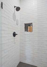 Roomy shower with full floor to ceiling tile walls, frameless glass door and a built in product alcove.
