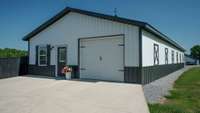 Opposite the home garage is the entrance to the outbuilding.  There is a garage door on both ends of this building rending the ability to drive through the outbuilding. It can serve to park multiple cars, store yard equipment and tools.