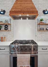 The cedar shiplap hood is flanked by farmhouse lights in addition to the recessed lights and island pendants.