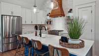 A brick backsplash and accent wall surrounds the white shaker cabinets with black hardware.