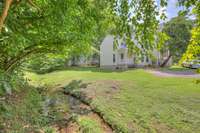 A picturesque setting with lush greenery, mature trees, and a charming natural creek running alongside the property. This tranquil environment provides both privacy and beauty, enhancing the home's relaxing atmosphere.