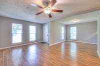 A spacious living area greets you with generous natural light streaming through large windows. The contemporary ceiling fan and warm tones of the flooring provide a comfortable, relaxed atmosphere ideal for relaxation and everyday living.