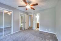 A serene bedroom featuring plush carpeting, contemporary ceiling fan, neutral walls, and abundant natural light. Its simplicity and spaciousness allow for versatile furniture placement and personalized décor.