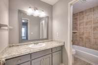 Modern and stylish bathroom featuring sleek cabinetry, updated vanity, and tasteful tile surrounding the bathtub-shower behind a door for privacy and function. Neutral tones provide a clean, refreshing environment.