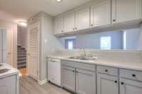 Opposite view of the kitchen highlighting ample storage, cabinet space, and countertop area. The opening to the living area ensures the cook remains connected to the activity in the adjoining rooms, creating an inclusive atmosphere.