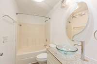 Primary bathroom with oversized tub/shower combo, updated vanities with granite countertops and glass sink.