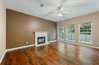 The fireplace and mantle are the focal point of the living room with pretty floors and ceiling fan.