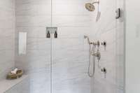 Primary Suite Bathroom with oversized zero entry shower. With frameless shower door, built in bench seat , wall niche, and detachable hand held shower head.