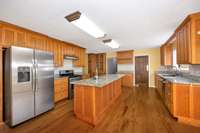 Kitchen - wood flooring, kitchen island, granite countertops, tile backsplash, stainless steel appliances, pantry