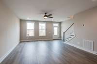 Expansive living room filled with natural light from two oversized windows, complete with outdoor access and a stylish fan light fixture for year-round comfort