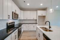Sleek and modern, this kitchen features classic all-white cabinetry with striking black hardware, stainless steel appliances, and a deep stainless steel sink.