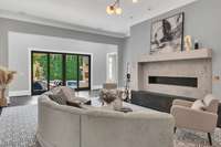 An elegant living room anchored by a striking fireplace, featuring soaring ceilings and expansive windows that fill the space with natural light — the perfect blend of warmth and grandeur.