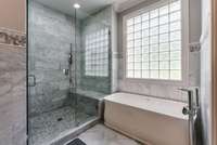 A luxurious master bath featuring a spacious walk-in shower and separate soaking tub, bathed in natural light streaming through elegant glass block windows.