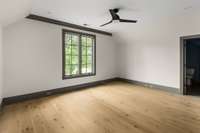 Upstairs you will find 3 additional bedrooms and bathrooms. This sunlit bedroom has a large window, rich wood flooring, and a fan light fixture—combining style, warmth, and functionality.