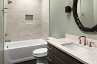 The attached well-appointed bathroom with a sleek vanity, quartz countertop, and a dual shower/bathtub also has hallway access for those enjoying the upstairs bonus room.