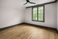 Another bright and comfortable bedroom featuring a large window, wood flooring, and a ceiling fan light fixture—designed for rest and relaxation.
