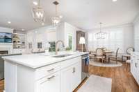 A peak of the oversized island w/ sink and the eating area with a wall of windows