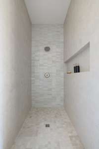 The suite includes a large walk-in shower with floor-to-ceiling tile and a long built-in shelf.