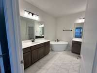 This primary bath is stunning! Warm stained cabinets and large format tile accented with black hardware. The separate vanities give you lots of space to spread out.