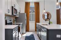 Modern, open layout kitchen features quartz counters, large island with seating for four, pantry and stainless appliances.