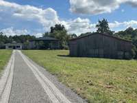 Entry to property shows barns to R and house on back mid portion of 6+ acre lot