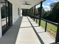 R side of house showing oversized covered porch and scenic view enabled wire railing with sliding glass door to kitchen area of great room with steps down to back yard and garage area at end