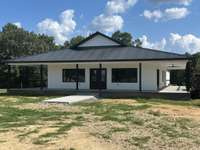 Front view of house showing 3 sides wraparound covered front porch. You can see the ceiling fan on R side of home amd sliding glass door to the kitchen/dining area of the great room