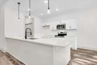 Gleaming white cabinets with white quartz top, stainless steel appliances and pendant lighting