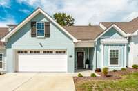 The soft blue, green, and white painted brick exterior sets a cheerful, waterfront tone while mature trees frame the entry.