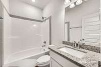 Stylish full bath with granite vanity, framed mirror, and tiled accents surrounding the tub-shower combo. A bright, polished space that feels both functional and refined.