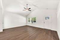 Spacious living room with vaulted ceiling and warm vinyl plank flooring. Large windows bring in natural light, offering a perfect blank canvas to style for cozy evenings or lively gatherings.