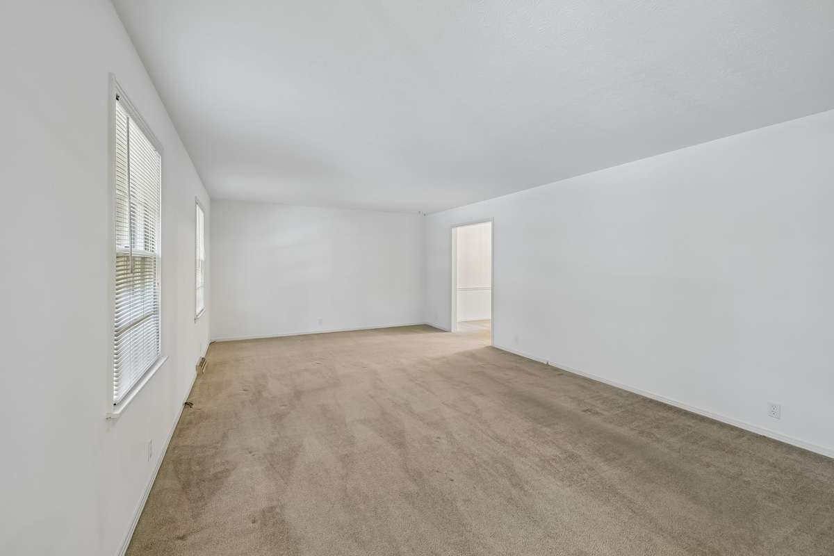 An expansive living room offers a serene retreat, featuring plush carpeting and large windows that frame views of the lush front lawn.