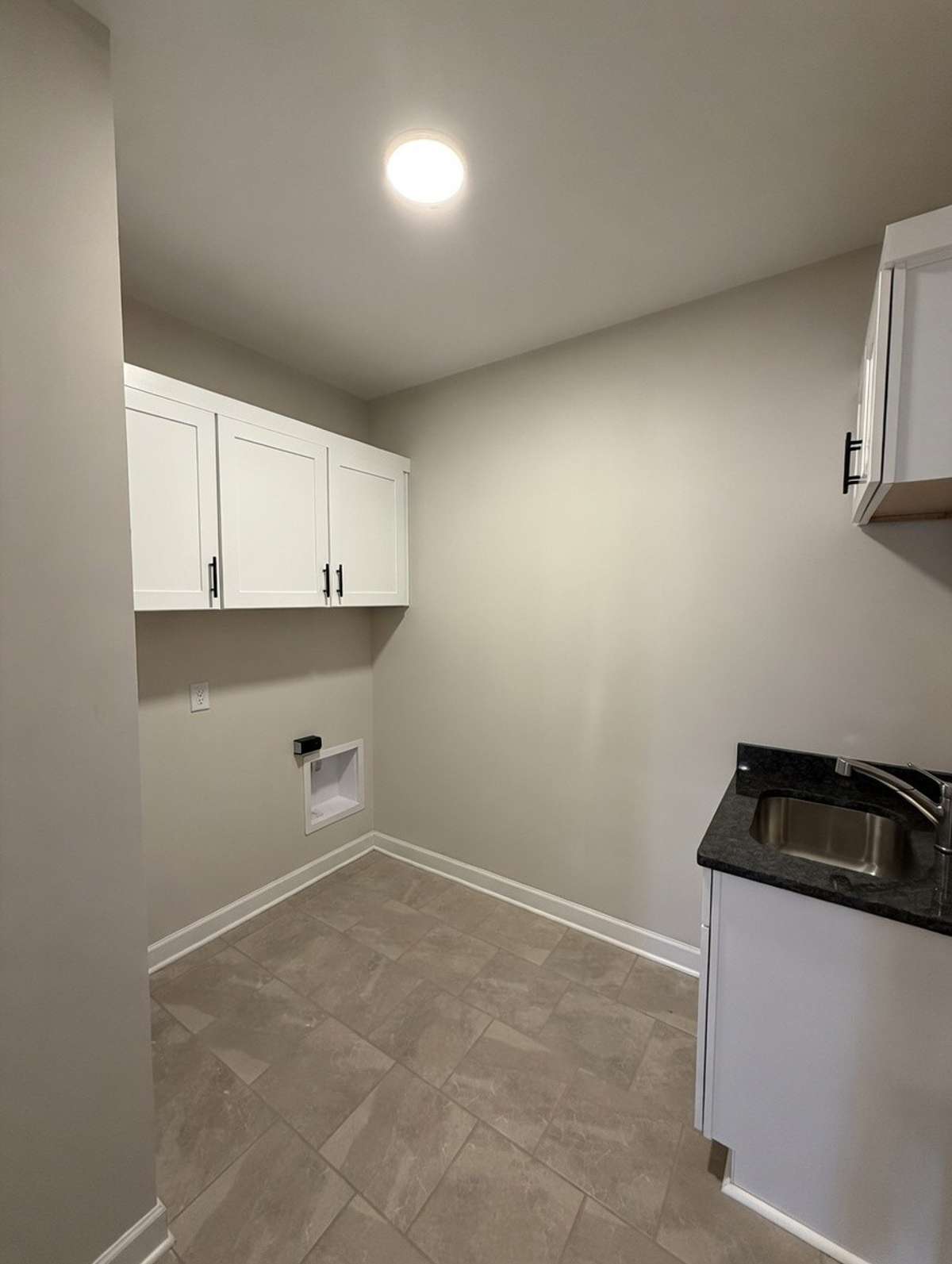 Large laundry room just outside the primary bedroom on the main level with cabinetry and sink with granite countertop