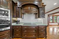 Detailed woodwork surrounds the stovetop with tile backsplash with stainless steel double ovens to the left.