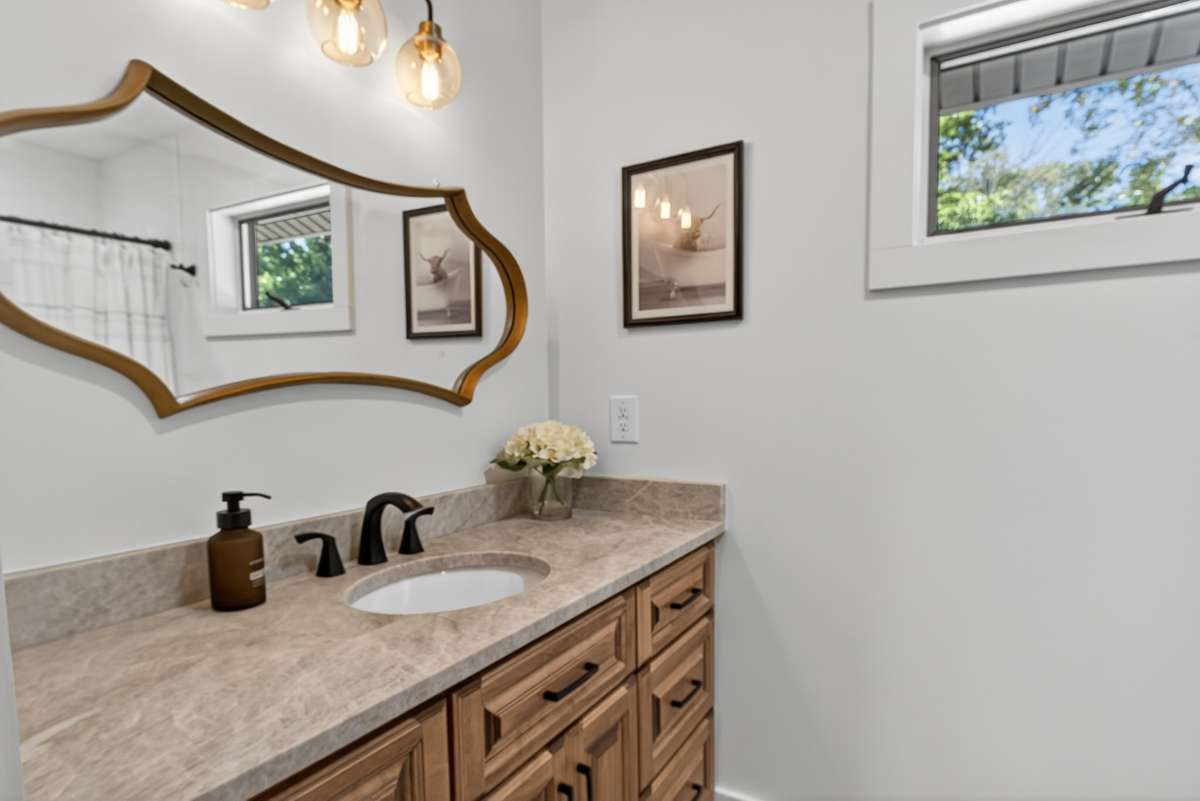 Hall bath features a custom wood vanity, Taj Mahal quartzite countertops and black accent hardware.