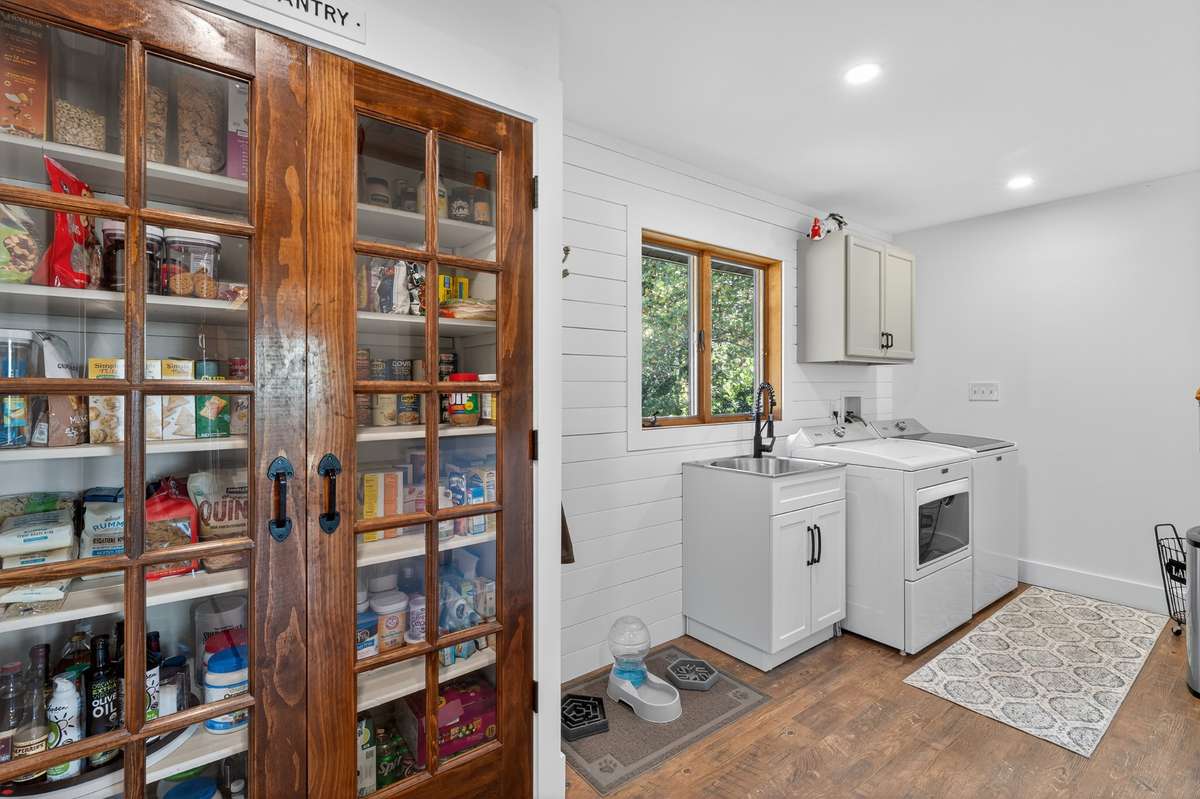 Laundry room is oversized and features storage cabinets and a laundry sink. Full size pantry with updated pantry doors and plenty of shelving for all your pantry needs.