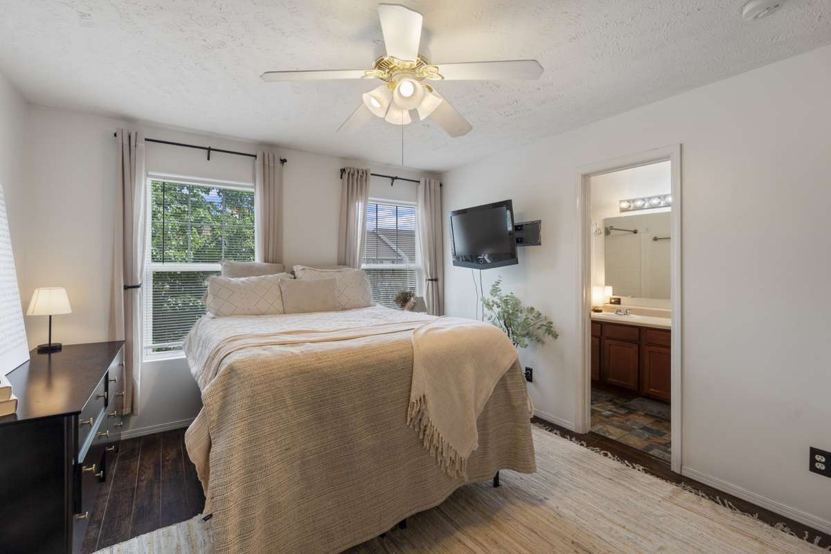 The primary bedroom features large picture windows, an upscale color scheme, and hardwood flooring.