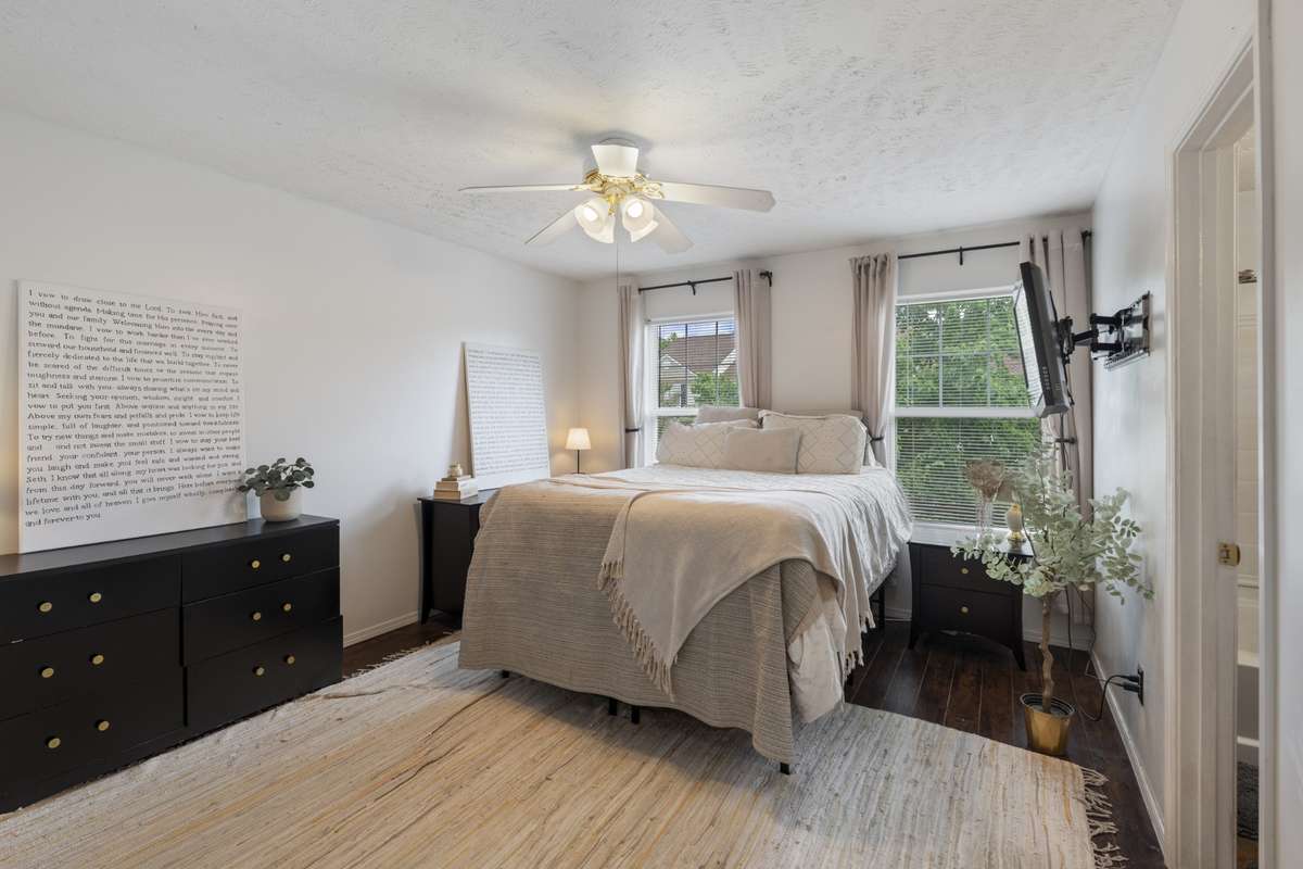 The primary bedroom features large picture windows, an upscale color scheme, and hardwood flooring.